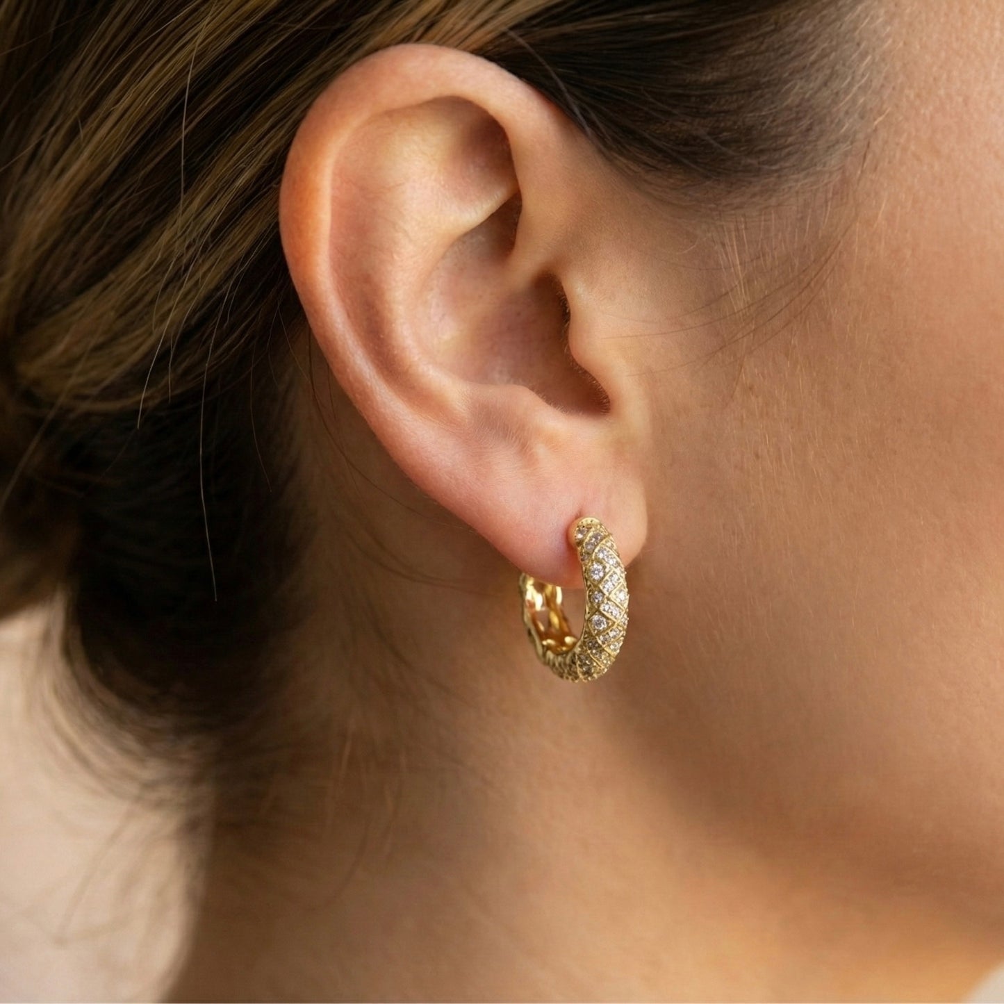 Close-up of an ear wearing a gold hoop earring with a blurred background
