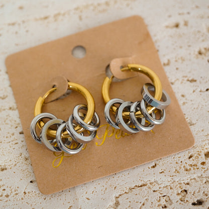 A pair of gold and silver hoop earrings with layered interlocking rings, displayed on a brown kraft paper card over a textured beige stone surface.