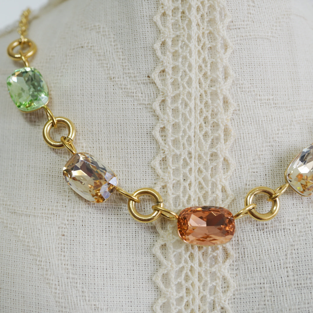 Close-up of sage green and peach cubic zirconia stones in a gold link chain.