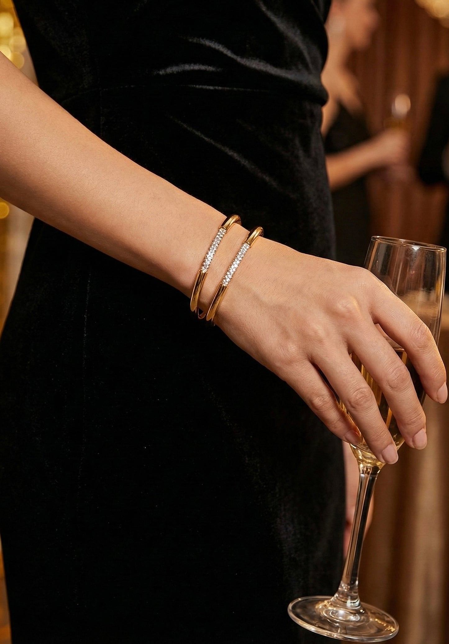 Model wearing Glow Petal Lumina gold bangles on wrist with black dress.. Luxury anti-tarnish stainless steel crystal cuff bracelet.