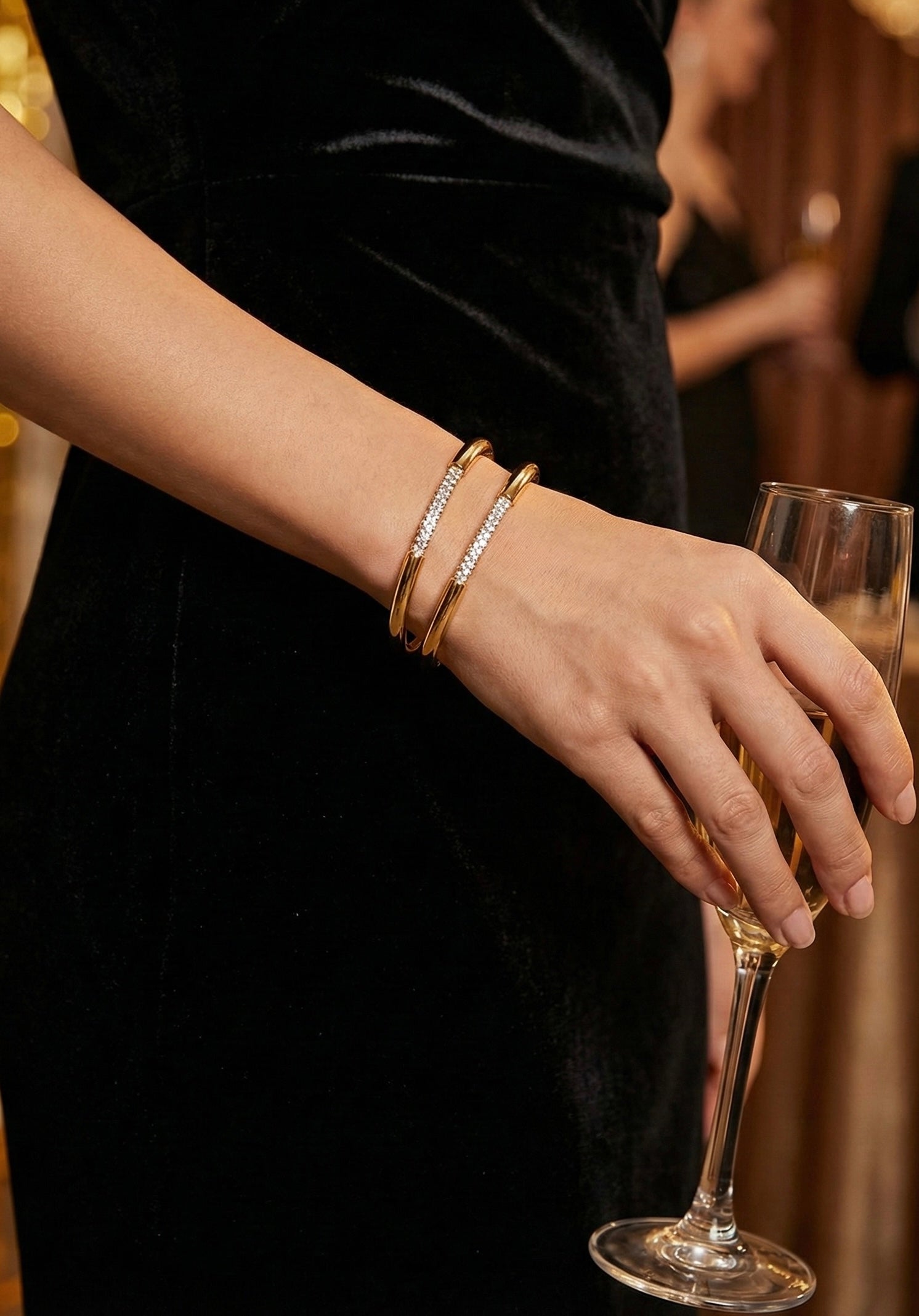 Model wearing Glow Petal Lumina gold bangles on wrist with black dress.. Luxury anti-tarnish stainless steel crystal cuff bracelet.