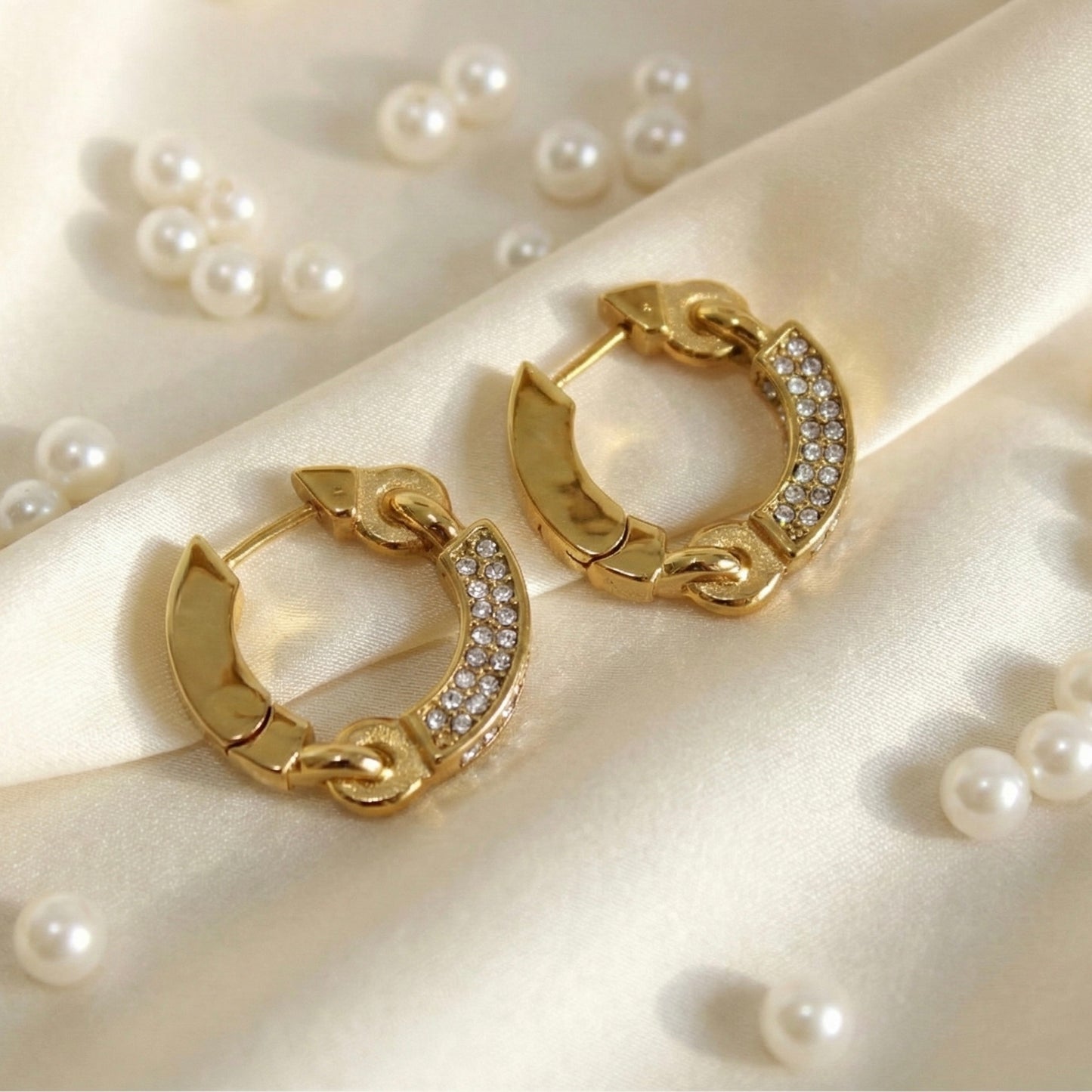 Gold huggie hoop earrings with crystal pave accents on a white satin background with pearls, luxury anti-tarnish jewelry.