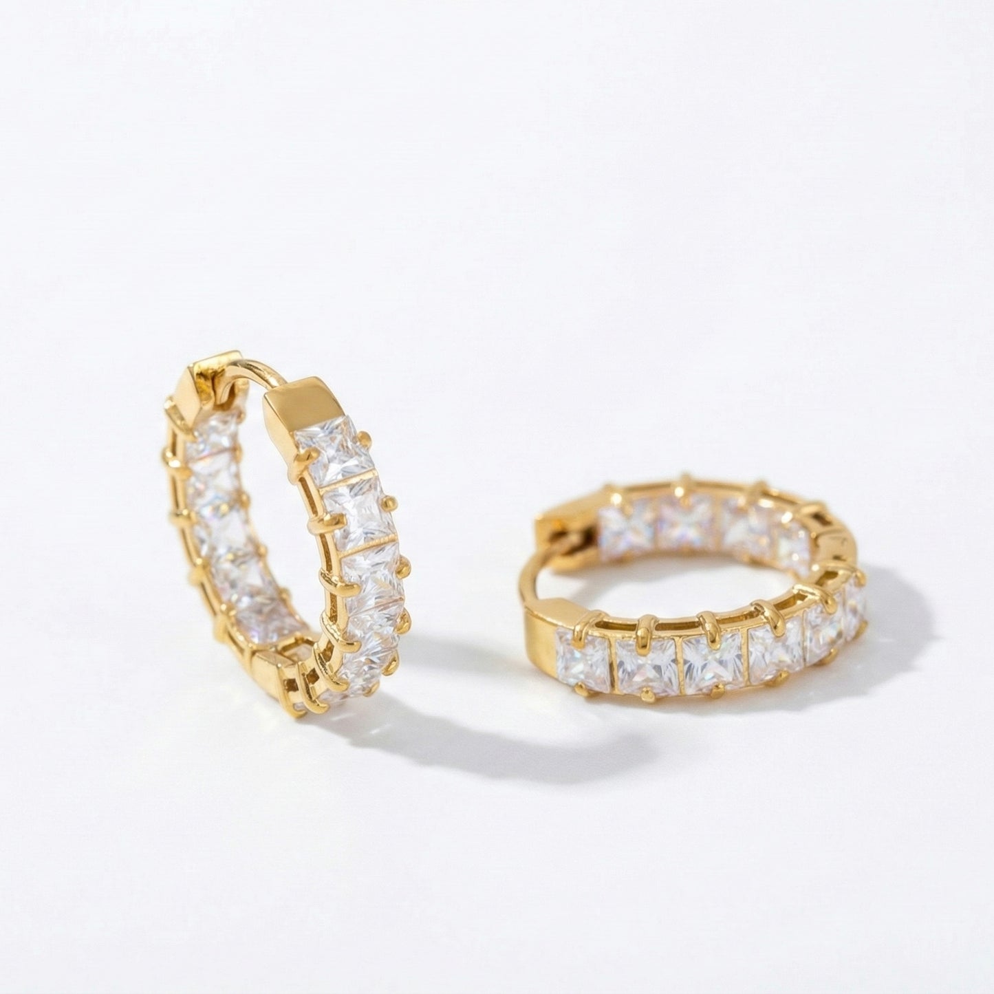 Pair of small gold huggie hoop earrings featuring a row of channel-set square-cut clear crystals, shown from a front and side angle on a white background.