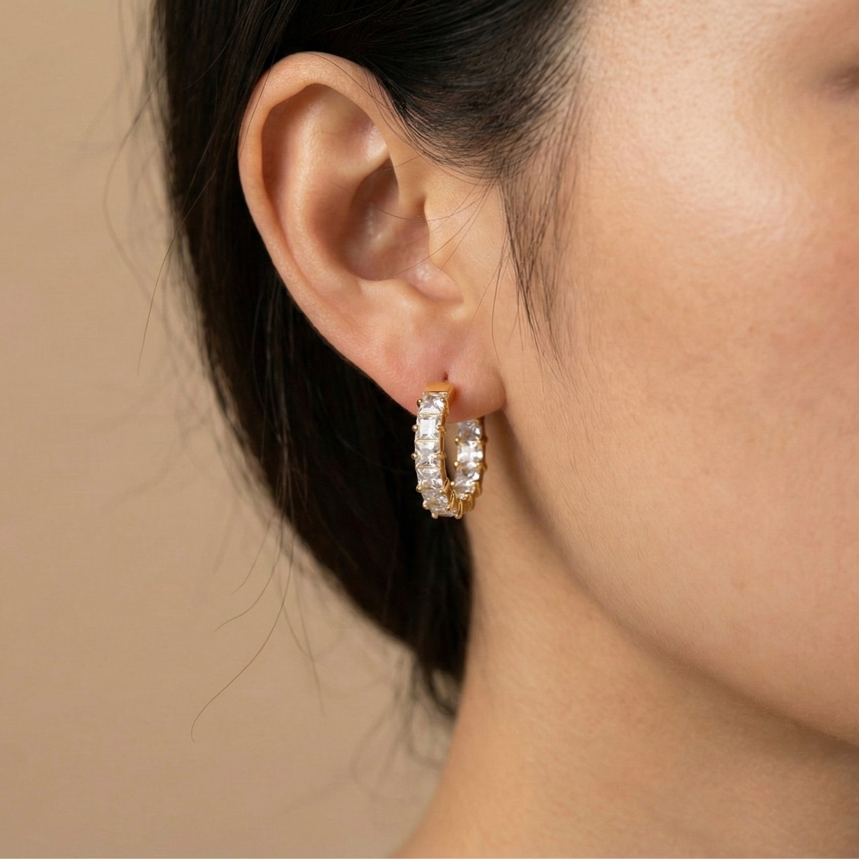 Close-up side profile view of a model's ear wearing a single gold square crystal huggie hoop earring showing size and fit.