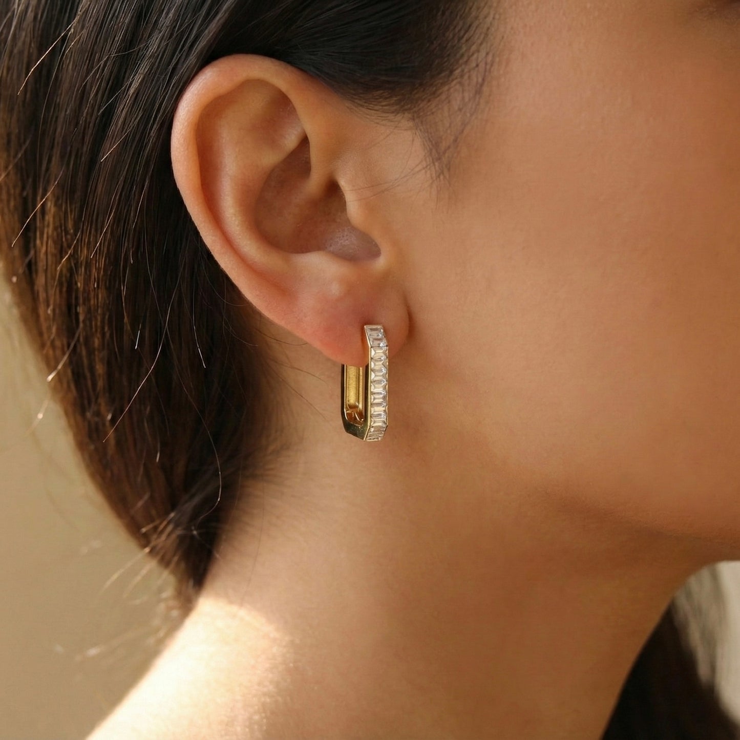 Close-up of an ear wearing a gold hoop earring with clear stones.