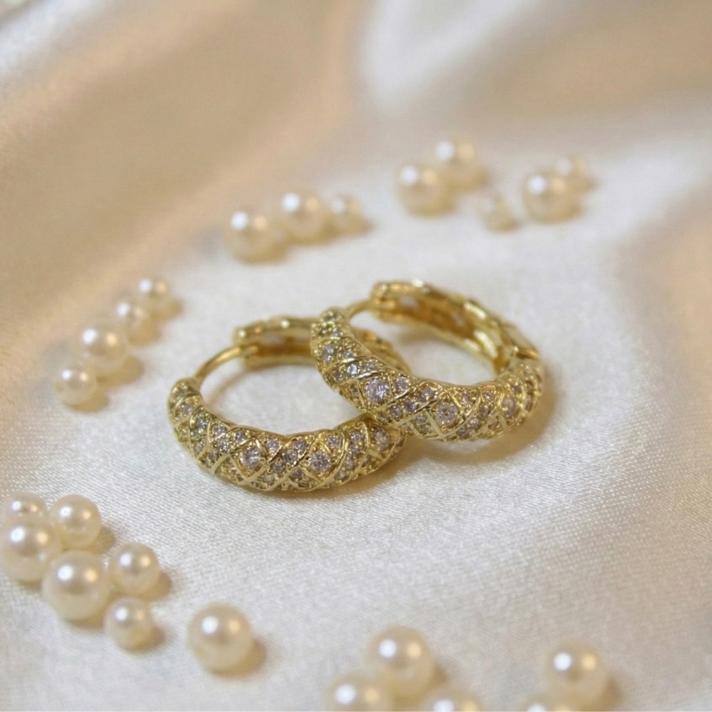 Gold hoop earrings with intricate designs on a bed of pearls.