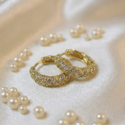 Gold hoop earrings with intricate designs on a bed of pearls.