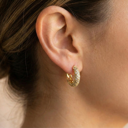 Close-up of an ear wearing a gold hoop earring with a blurred background