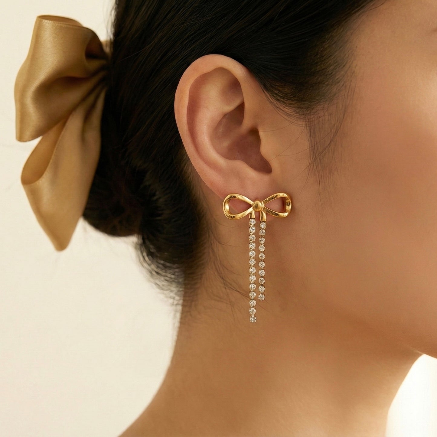 Gold bow earring with dangling crystals worn by a person with a gold bow in their hair.