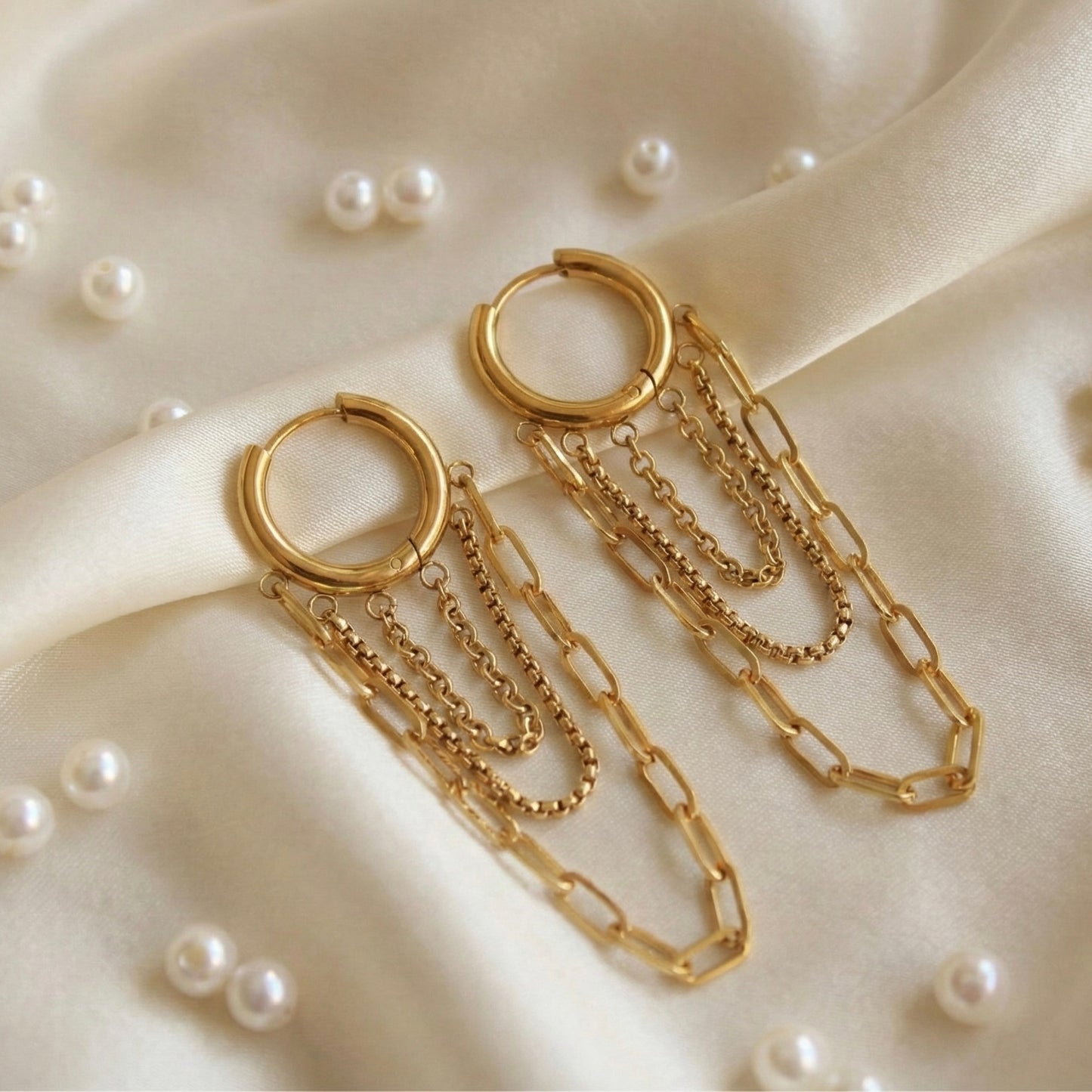 Gold hoop earrings with chains on a beige fabric background with pearls.