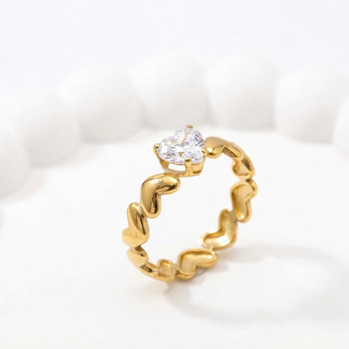 Gold anti-tarnish ring with heart-shaped crystal on a white aesthetic tray.
