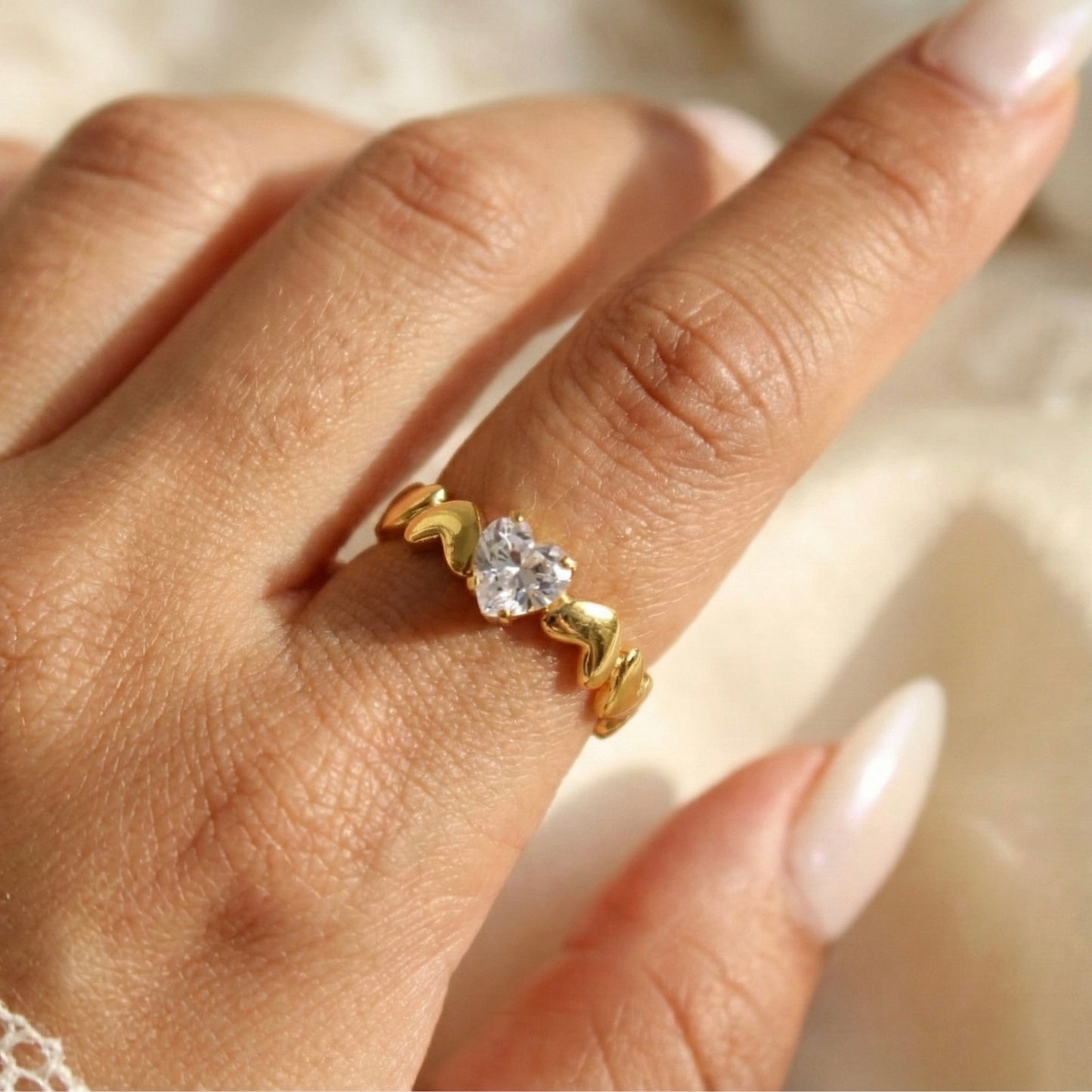 Gold ring with a diamond on a person's finger against a neutral background