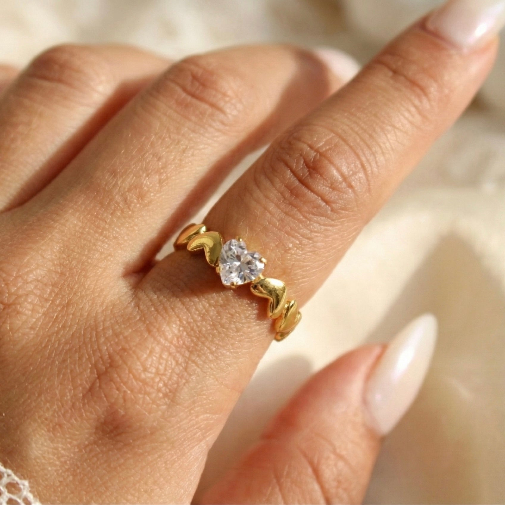 Gold ring with a diamond on a person's finger against a neutral background