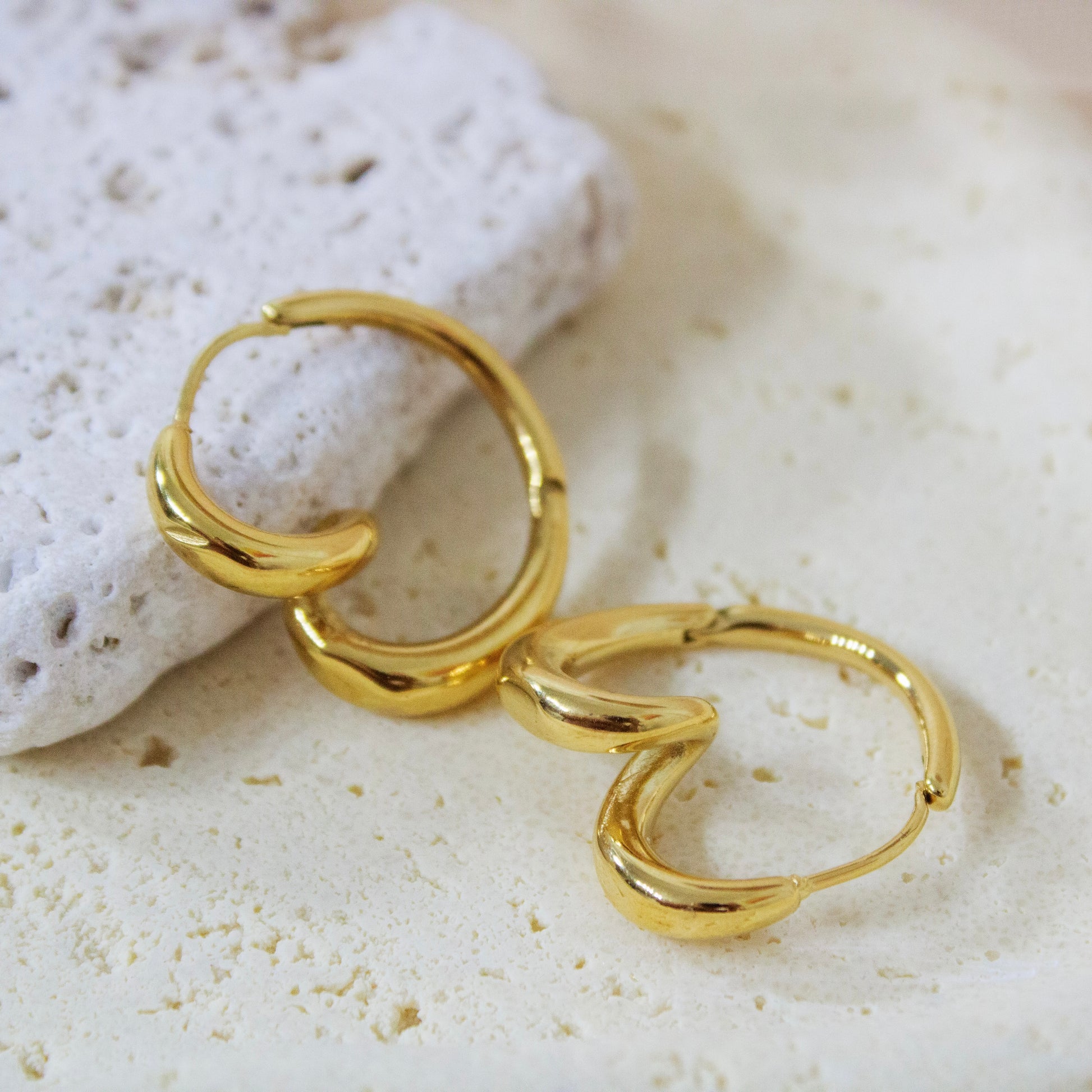 Gold twisted hoop earrings on white stone prop, anti-tarnish jewelry.