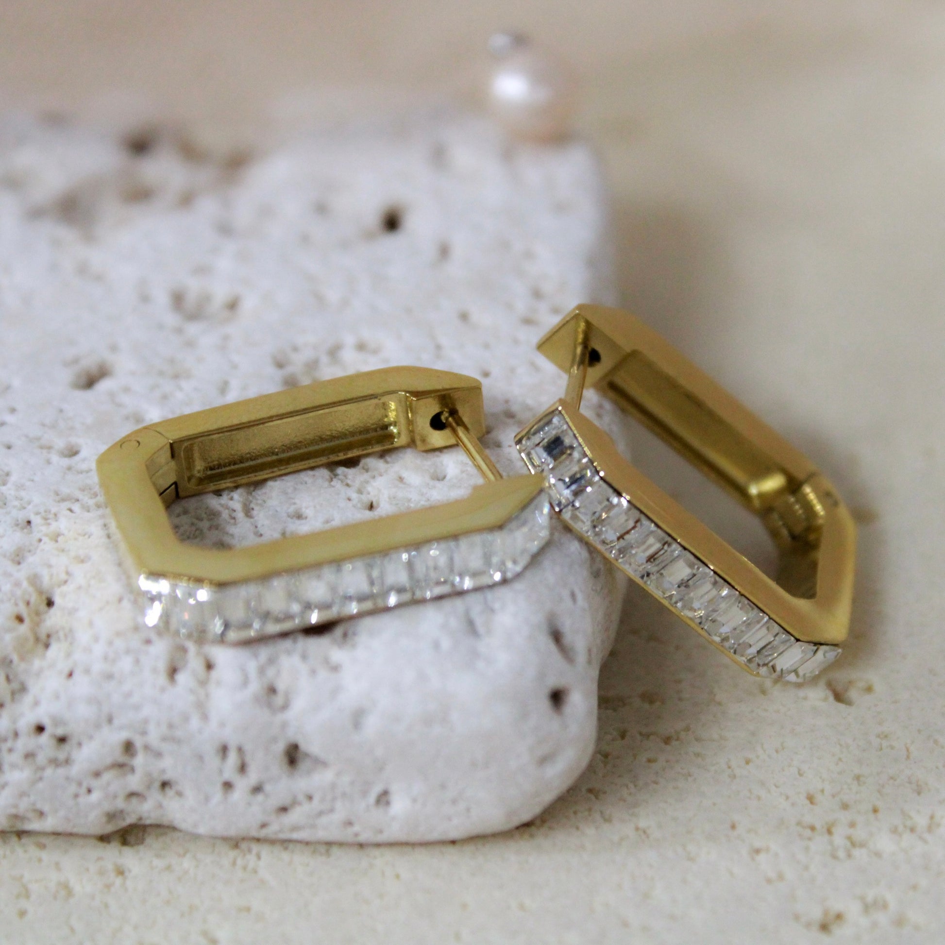 Gold rectangular hoop earrings with baguette diamonds standing on stone prop.