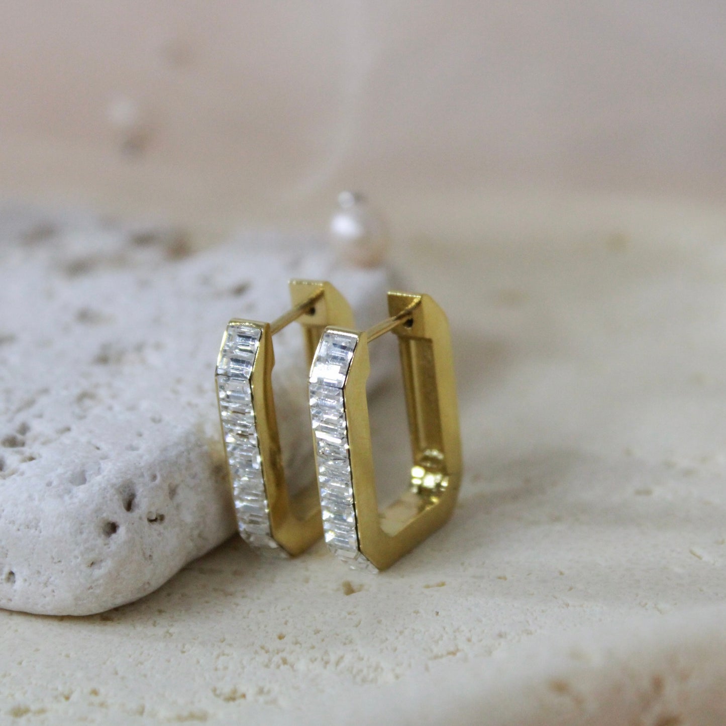 Gold hoop earrings with clear stones on a textured stone surface