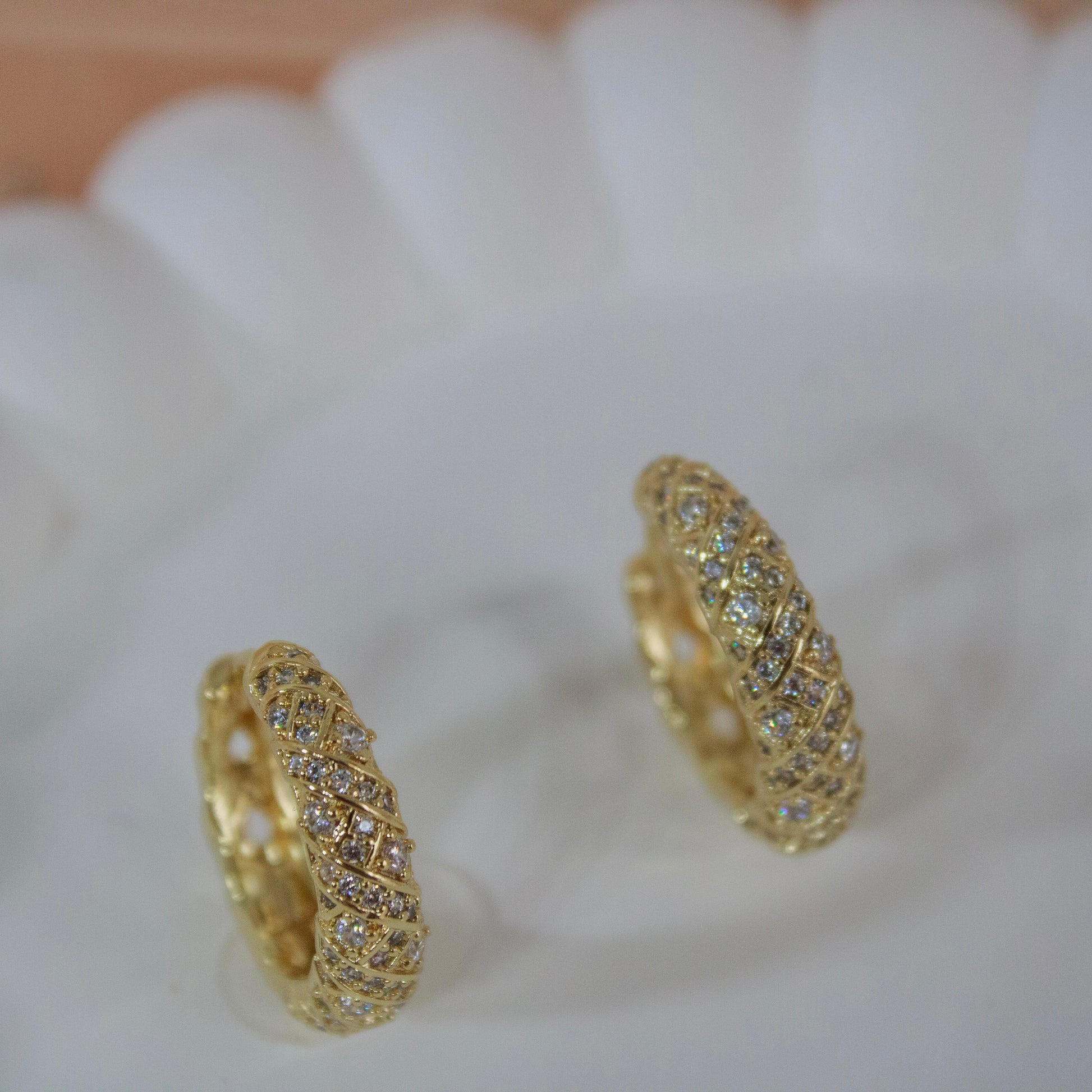 Gold huggie earrings with criss cross diamond pattern on white plate