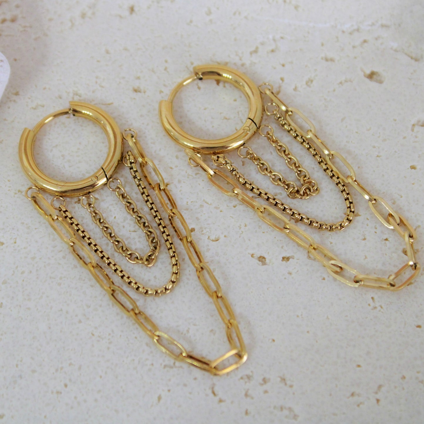 Gold hoop earrings with chain extensions on a light background