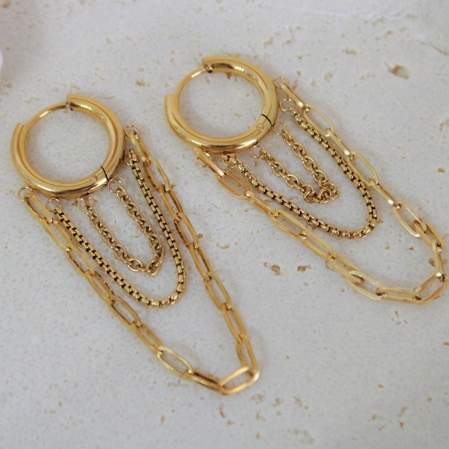 Gold hoop earrings with chain extensions on a light background