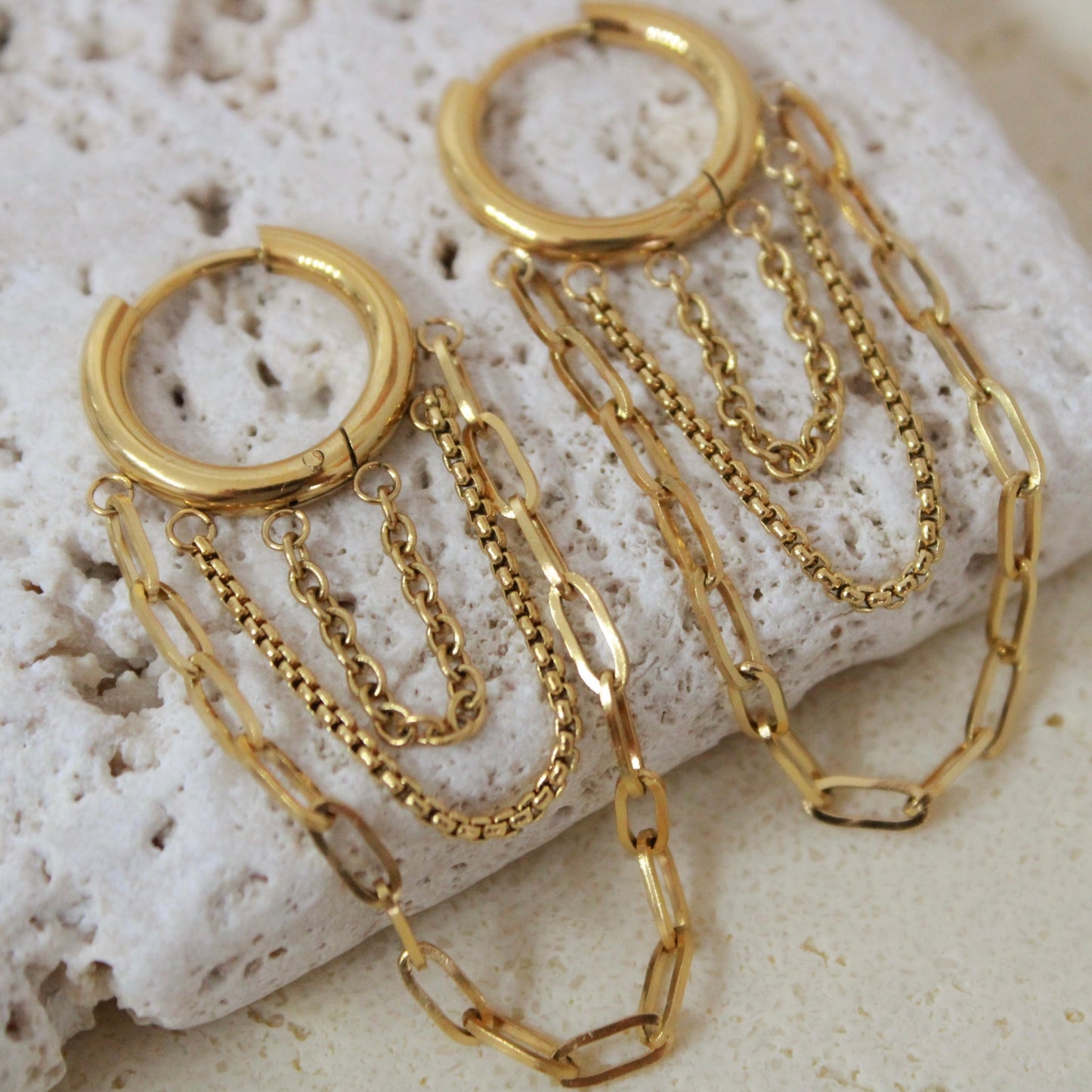 Gold hoop earrings with chain details on a textured stone surface