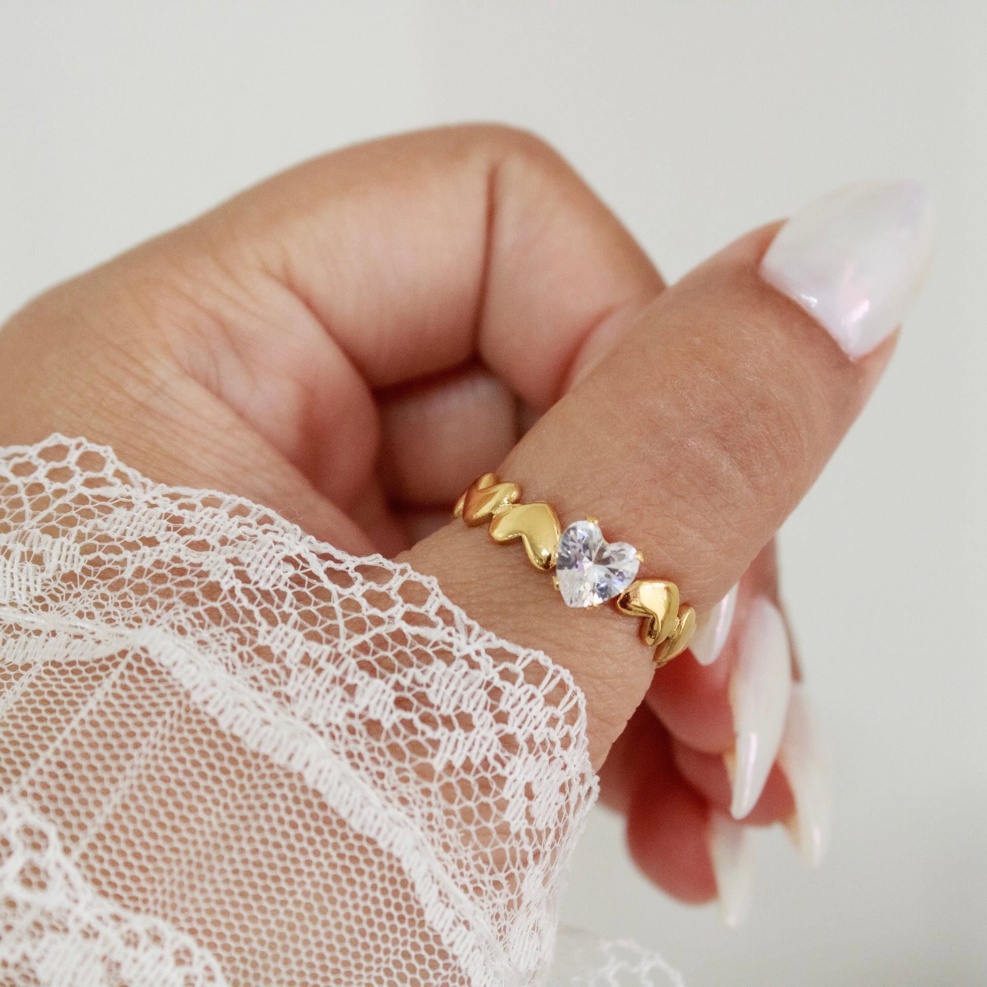 Woman wearing gold heart ring on middle finger with white lace sleeve.
