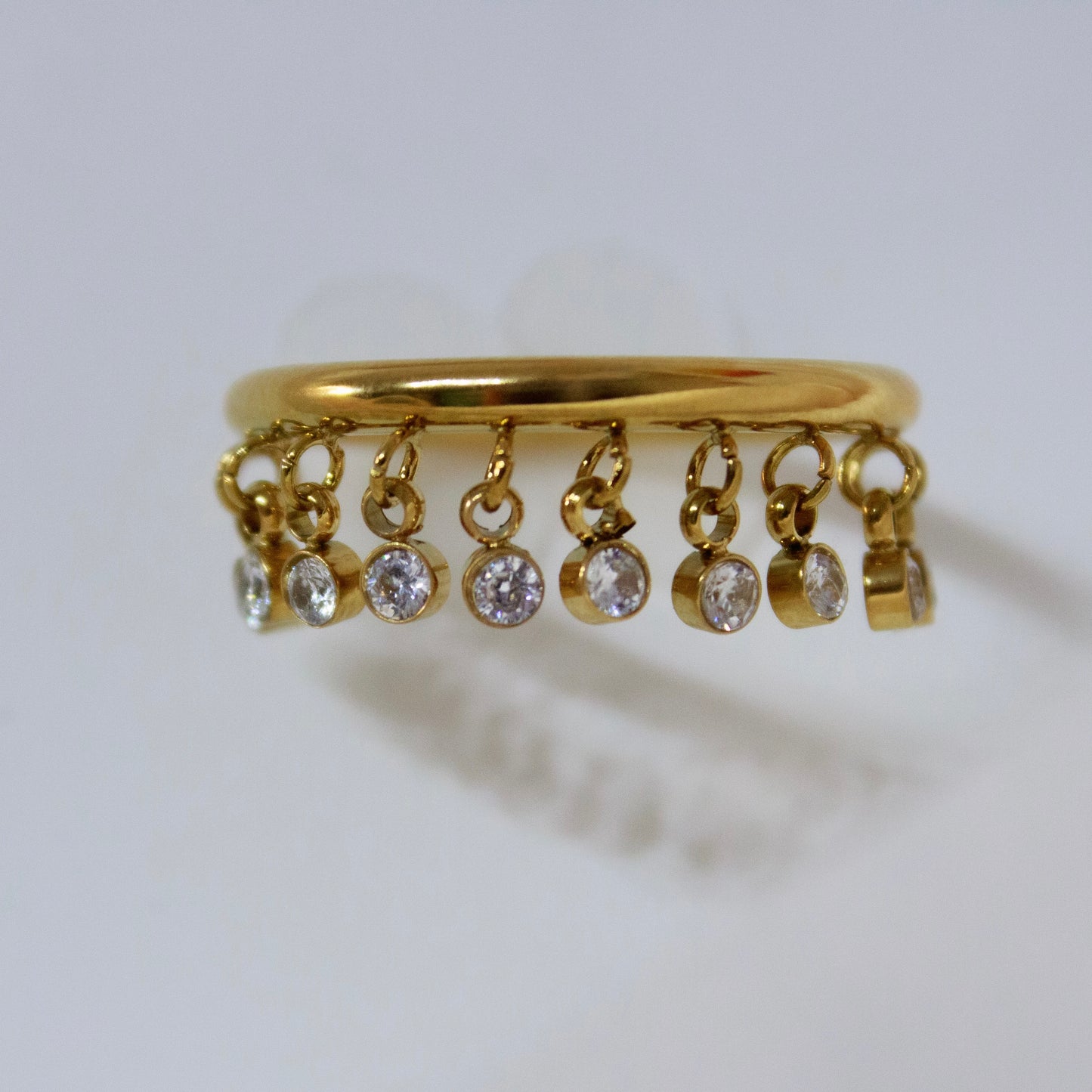 Gold anti-tarnish ring with dangling crystal charms on white stand.