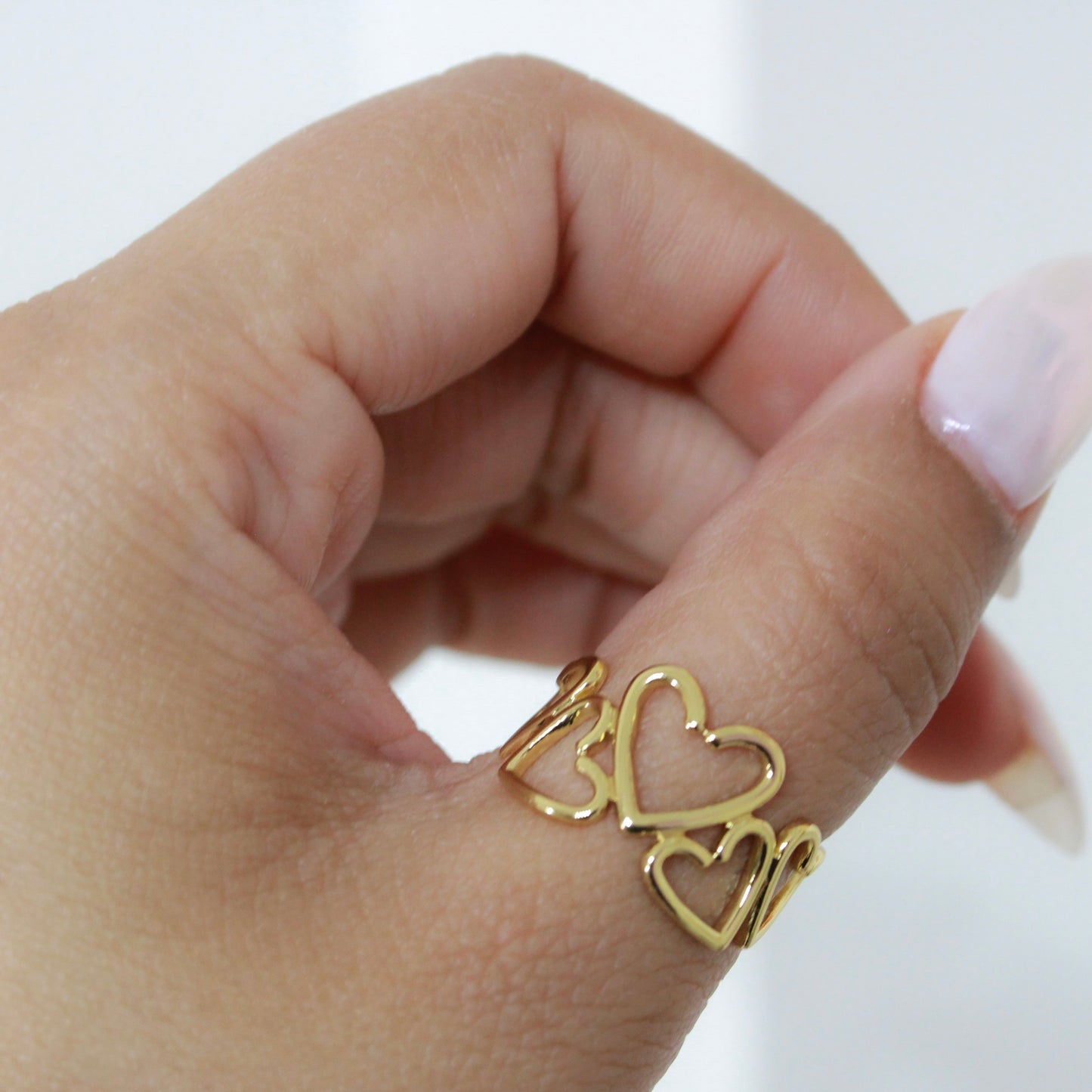 Gold heart-shaped ring on a person's finger against a white background
