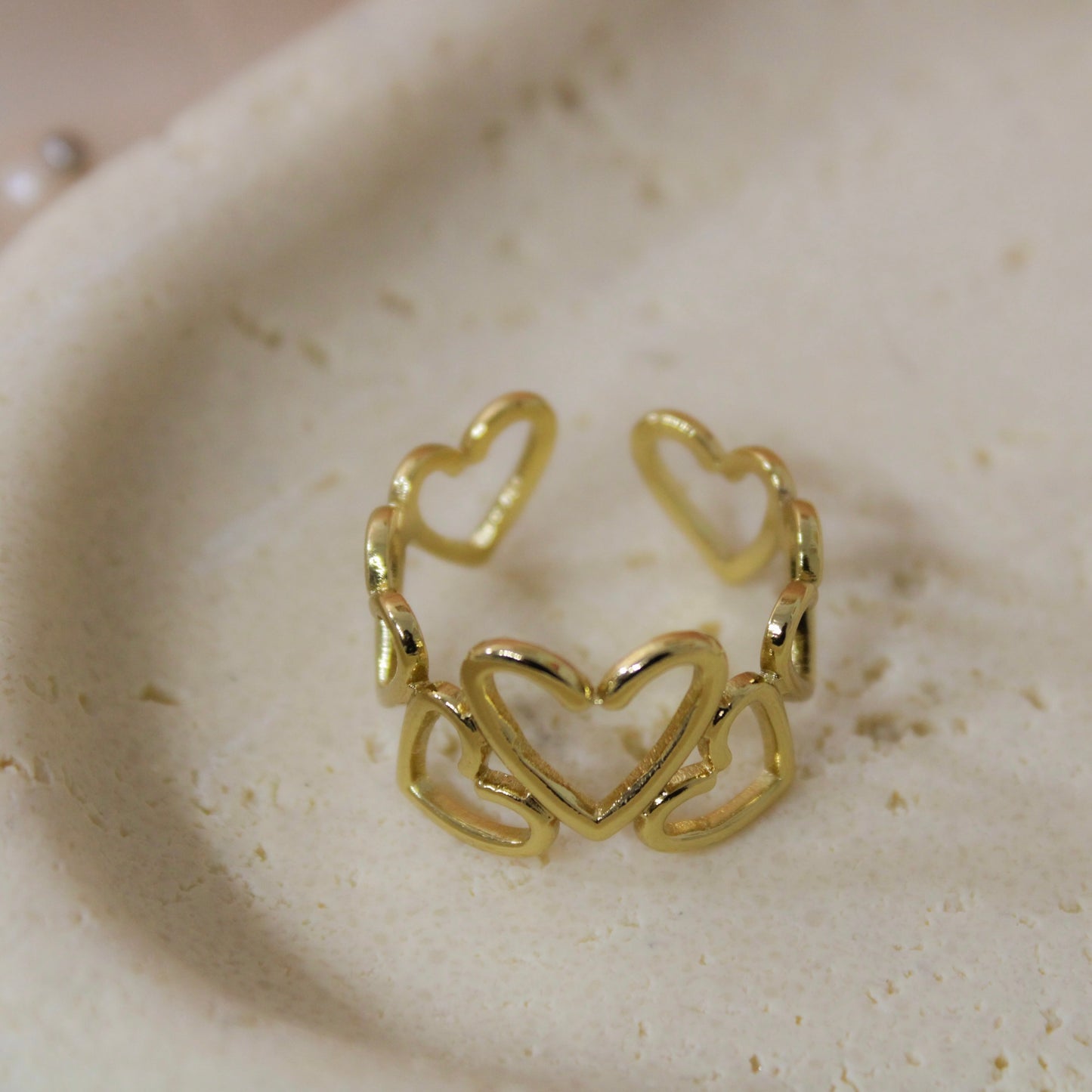 Gold heart-shaped ring on a textured beige surface