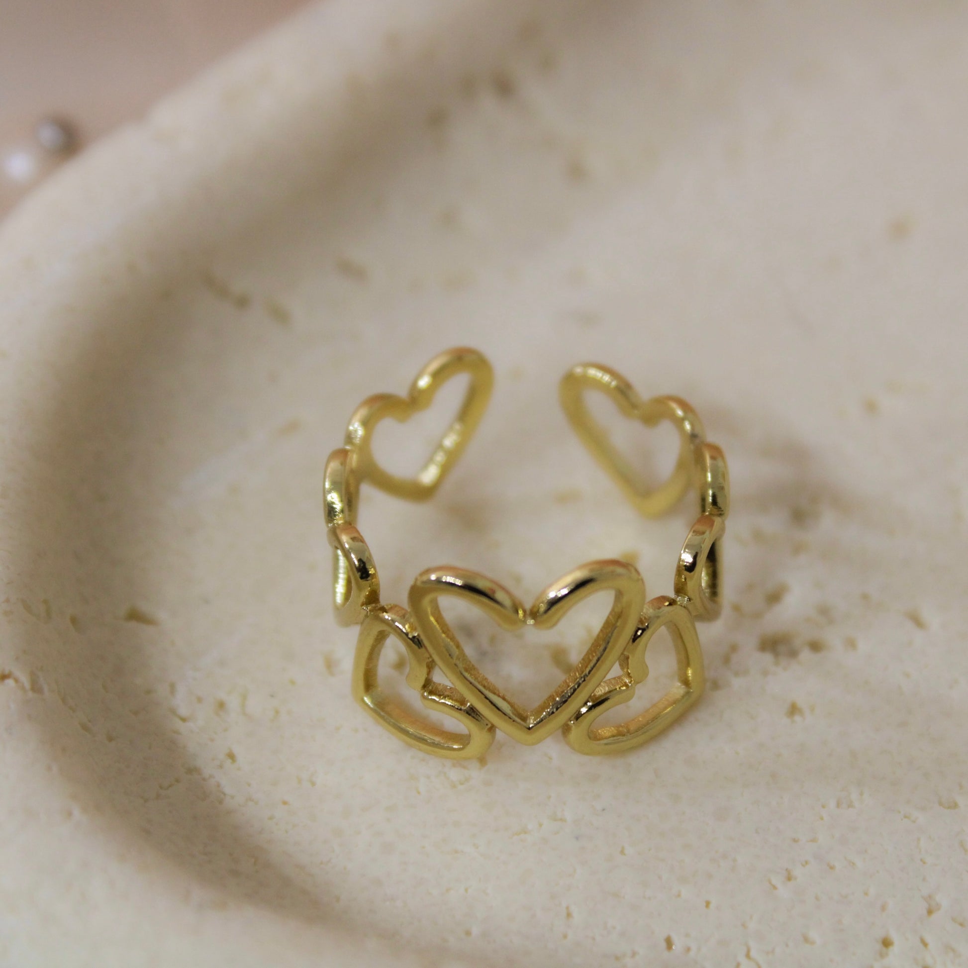 Gold heart-shaped ring on a textured beige surface