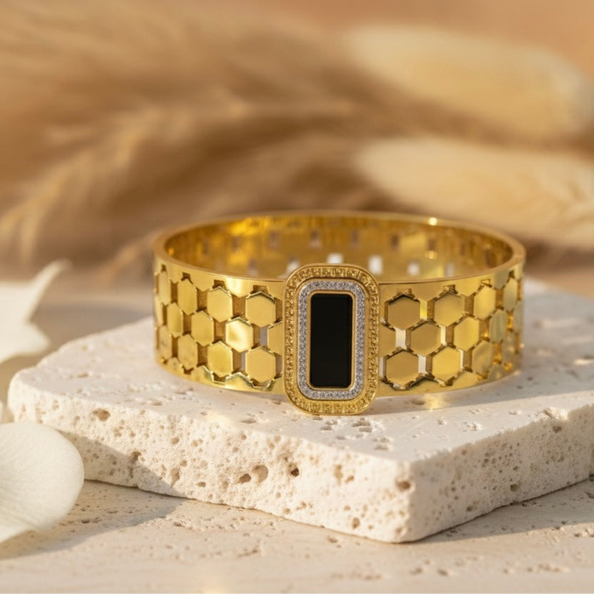 Gold bracelet with hexagonal pattern on a textured stone surface