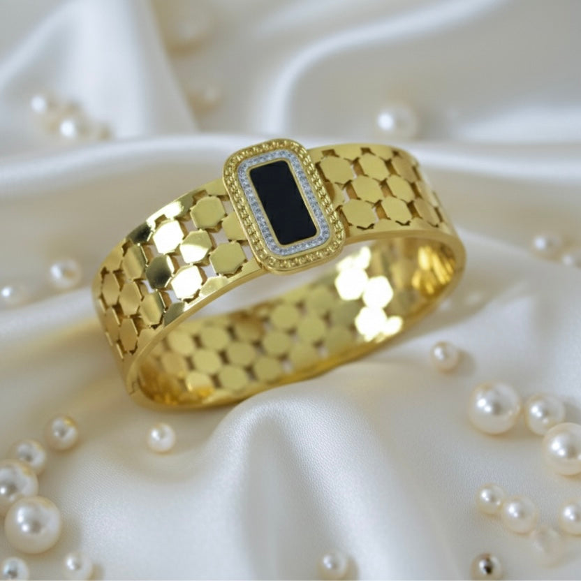 Gold bangle with a black center on a white fabric background with pearls
