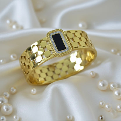 Gold bangle with a black center on a white fabric background with pearls